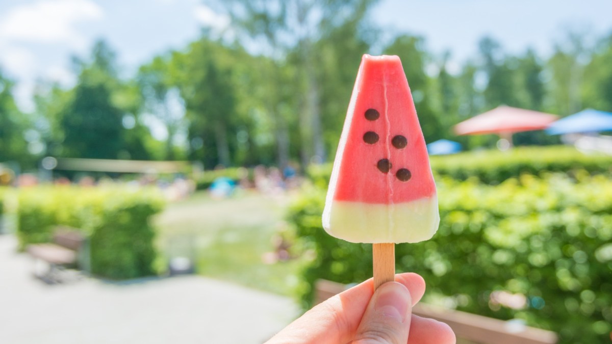 Snacks Freibad: Jemand hält im Freibad ein Eis am Stiel vor sich hoch.