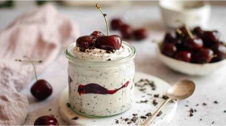 Ein Glas mit Stracciatella-Quark mit Kirschkompott, Schale mit frischen Kirschen im Hintergrund