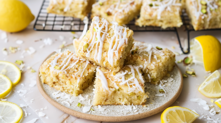 Zitronen-Kokos-Blondies auf einem Teller. Als Dekoration liegen einige Zitronenscheiben außen herum.