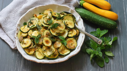 Ein Teller Zucchini alla Scapece, daneben Minzblätter und gelbe und grüne Zucchini.