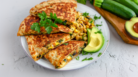 Zucchini-Tortillas auf einem Teller, angerichtet mit Rührei und Avocado.