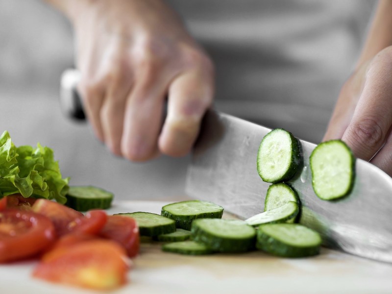 ZWILLING selbstschärfender Messerblock: Ein Ausschnitt, auf dem jemand ein Messer in der Hand hält und Gurke damit schneidet. Auf dem Brett liegen Gurkenscheiben, Tomatenscheiben und Salat. Der Hintergrund ist verschwommen.