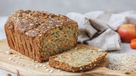 Ein angeschnittenes Apfel-Möhren-Brot auf einem Holzbrett.