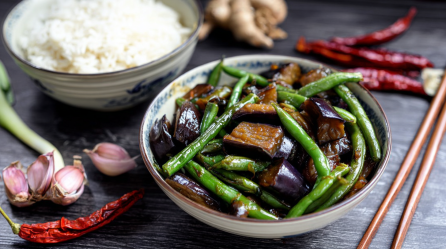 Eine Schale Auberginen-Bohnen-Stir-Fry, serviert mit einer Schale Reis.