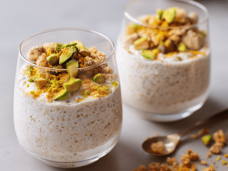 Zwei Gläser mit Baklava Overnight Oats. Daneben liegt ein kleiner Löffel und etwas Nuss-Crunch.