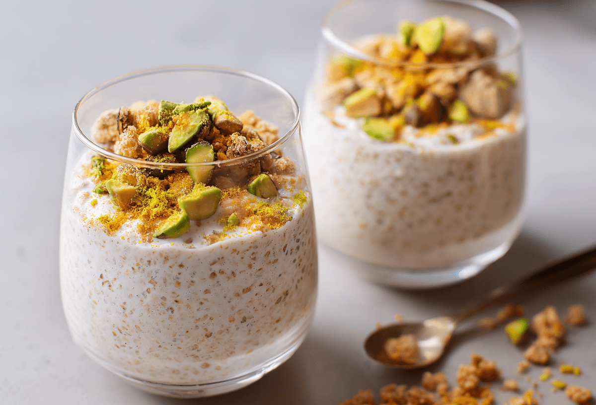 Zwei Gläser mit Baklava Overnight Oats. Daneben liegt ein kleiner Löffel und etwas Nuss-Crunch.
