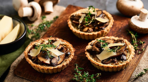 Drei Champignon-Tartelettes auf einem Holzbrett.