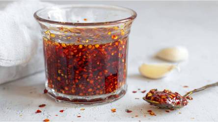 Glas mit Crispy Chili-Öl, Knoblauchzehen im Hintergrund