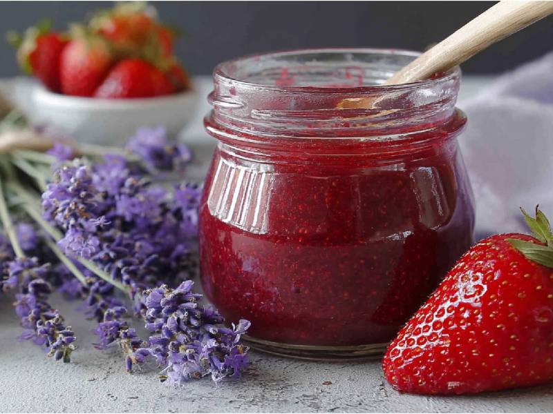 Glas mit Erdbeer-Lavendel-Marmelade auf einem Tisch, Strauß Lavendel und frische Erdbeeren daneben
