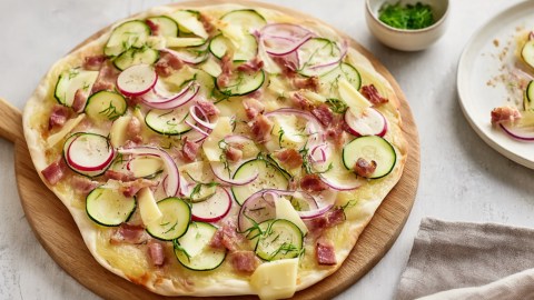 Ein Flammkuchen mit Zucchini vom Grill auf einem Holzbrett.