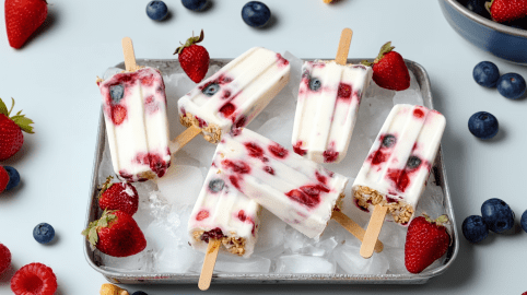 Sechs Frühstückseis liegen auf einer, mit Eiswürfeln gefüllten Form. Drumherum verteilt liegen Blau- und Erdbeeren.
