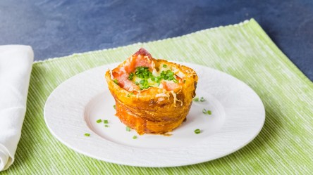 Ein gefüllter Croissant-Muffin steht auf einem weißen Teller und ist mit Schnittlauch bestreut. Der Teller steht auf einer grünen Unterlage.