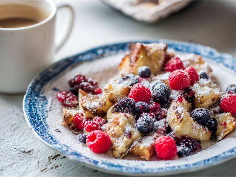 Teller mit Haferflocken-Kaiserschmarrn und einer Tasse Kaffee im Hintergrund