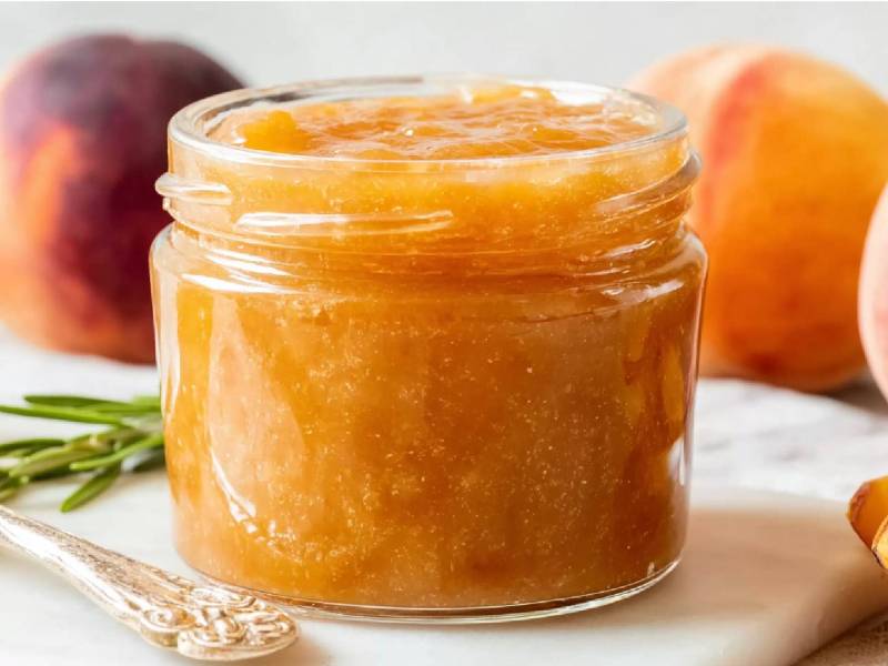 Glas Pfirsich-Rosmarin-Marmelade mit frischen Pfirsichen im Hintergrund