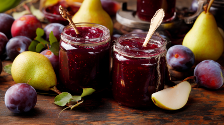 Zwei Gläser mit Pflaumen-Birnen-Marmelade. In den Gläsern stecken Löffel, außen herum liegt frisches Obst.