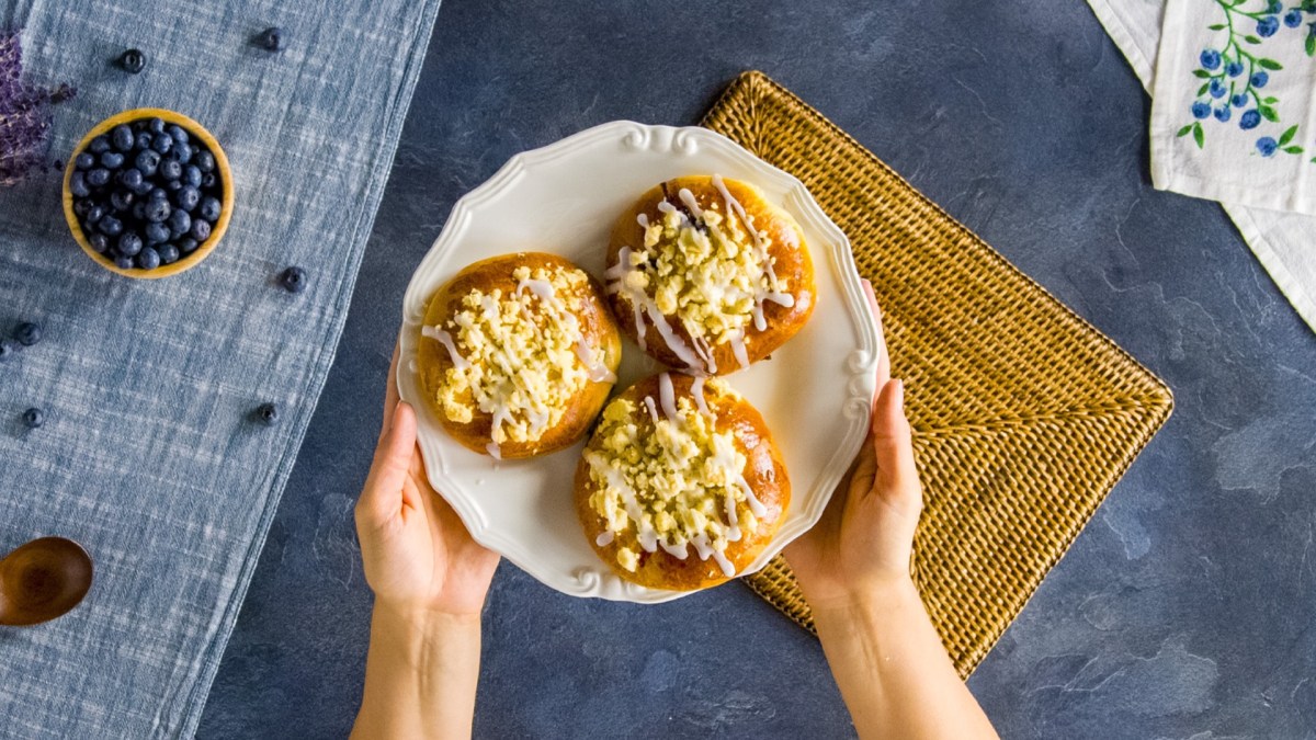Drei polnische Blaubeerbrötchen auf einem Teller, der von zwei Händen gehalten wird.
