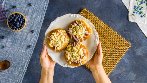 Drei polnische Blaubeerbrötchen auf einem Teller, der von zwei Händen gehalten wird.