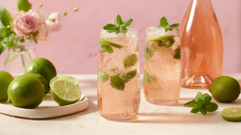 Zwei Gläser mit Sommerschorle mit Rosé, daneben stehen Limetten und eine Flasche Rosé.