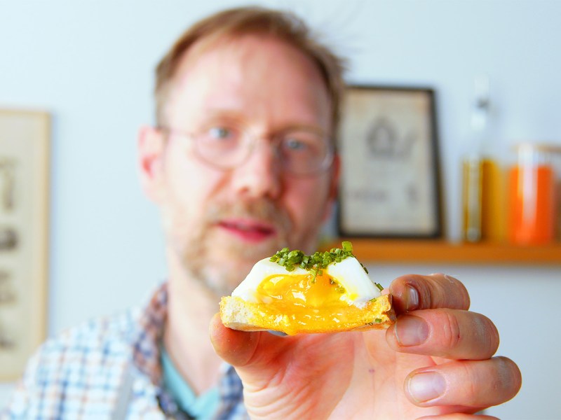 Pochiertes Ei auf einem Toast in einer Hand gehalten