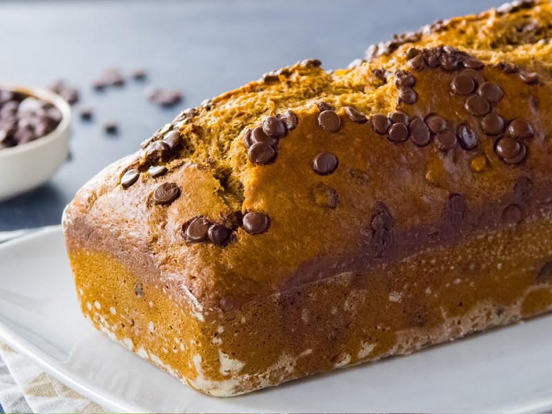 Veganes Bananenbrot mit Nüssen und Schoko-Drops, serviert auf einem Tablett. Im Hintergrund steht eine Schale mit Schoko-Drops.