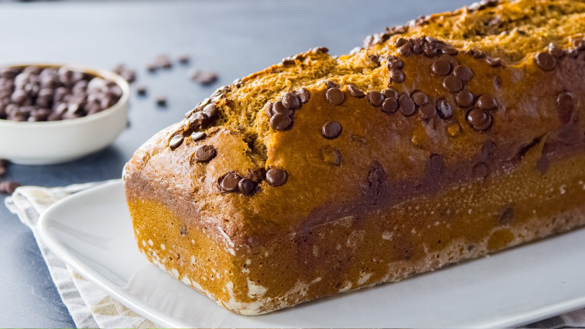 Veganes Bananenbrot mit Nüssen und Schoko-Drops, serviert auf einem Tablett. Im Hintergrund steht eine Schale mit Schoko-Drops.
