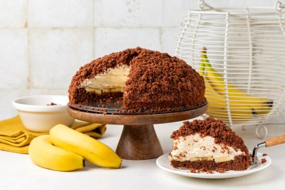 Ein veganer Maulwurfkuchen auf einem Präsentierteller. Ein Stück ist herausgeschnitten und gibt den Blick auf die Füllung frei. Davor und dahinter liegen insgesamt vier Bananen.