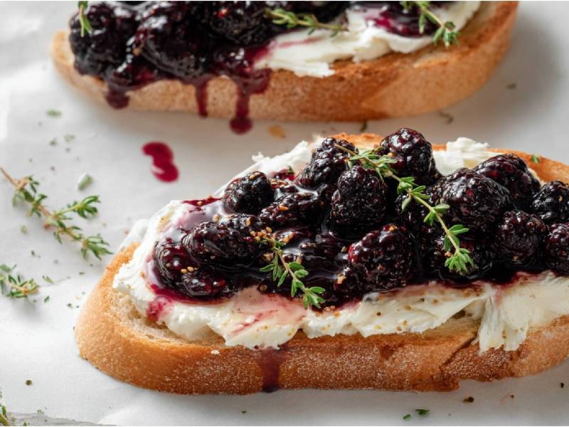 Zwei Ziegenkäse-Stullen mit geschmolzenen Brombeeren auf einem Tisch