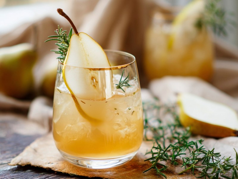 Ein Glas Birnen-Ingwer-Lillet mit Zimt. Rosmarinzweige und Birnenstücke sind zu sehen.