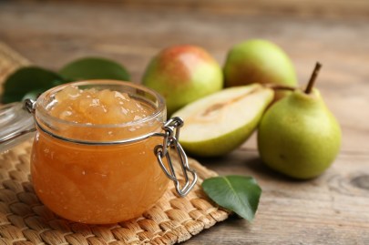 Ein Glas mit Birnen-Marzipan-Marmelade steht auf einem Platzdeckchen. Im Hintergrund sind Birnen zu sehen.