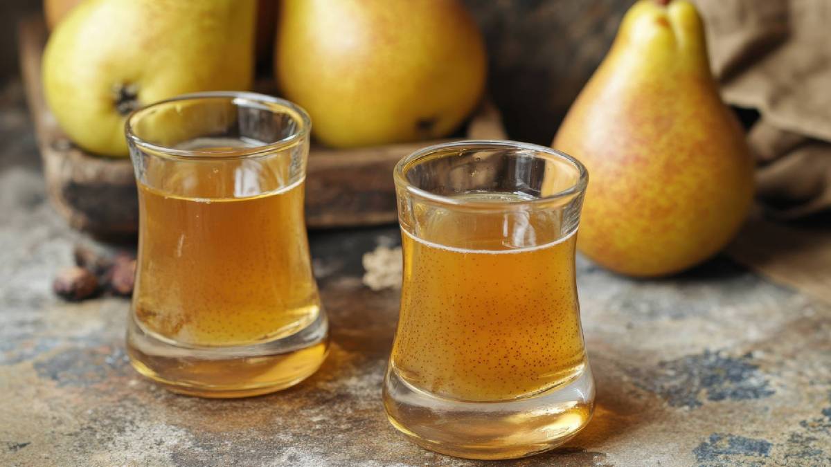 Zwei Schnapsgläser mit selbst gemachtem Birnenlikör auf einem Tisch, frische Birnen dahinter