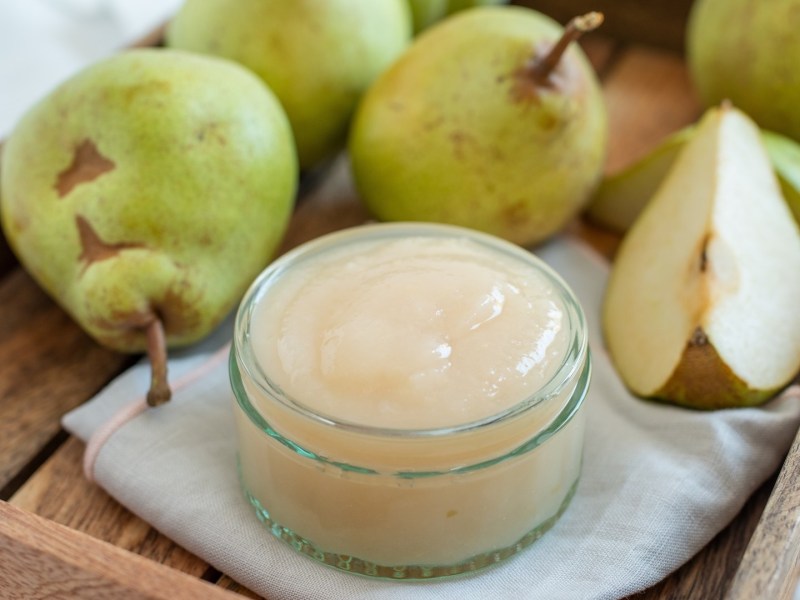 Ein Glas Birnenmus zwischen frischen Birnen.