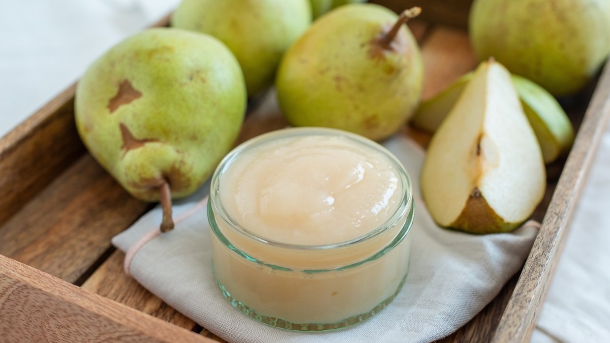 Ein Glas Birnenmus zwischen frischen Birnen.