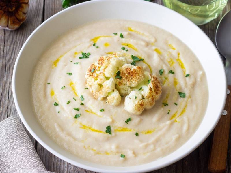 Eine Schüssel mit Blumenkohl-Bohnen-Suppe, garniert mit geröstetem Blumenkohl.