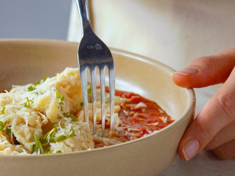 Nahaufnahme: Ein Teller mit Brotpasta mit Tomatensoße und geriebenem Hartkäse serviert.