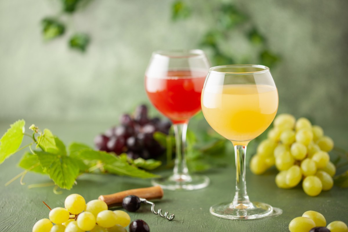 Zwei Gläser mit Federweißer und Federroter sind zu sehen. Darum liegen helle und dunkle Weintrauben.