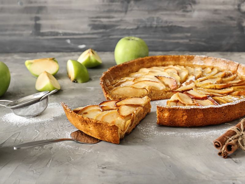 Eine Haferflocken-Apfel-Tarte mit einigen Äpfeln auf einer Arbeitsfläche.