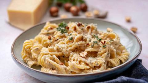 Ein Teller Haselnuss-Pasta mit Haselnüssen und Parmesan im Hintergrund