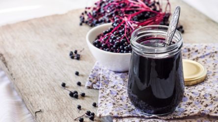 Ein Glas Holunderbeersaft. Daneben eine Schale mit Holunderbeeren.