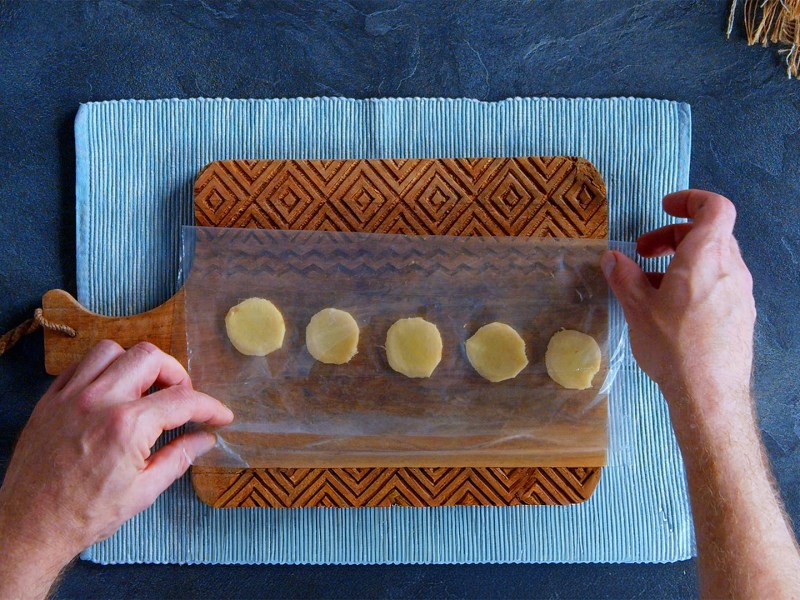 Ein Holzbrett, auf dem ein Gefrierbeutel mit Ingwerscheiben platziert ist.