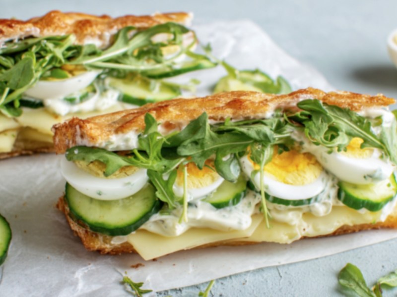 Zwei Kartoffelsandwiches mit Ei, Gurke, Käse und Rucola.