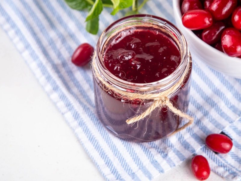 Ein Glas Kornelkirschen-Marmelade, daneben eine Schale mit Kornelkirschen.