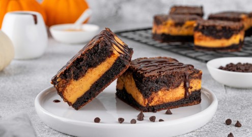 Zwei Kürbis-Cheesecake-Brownies auf einem Teller. Der Rest ist im Hintergrund zu sehen.