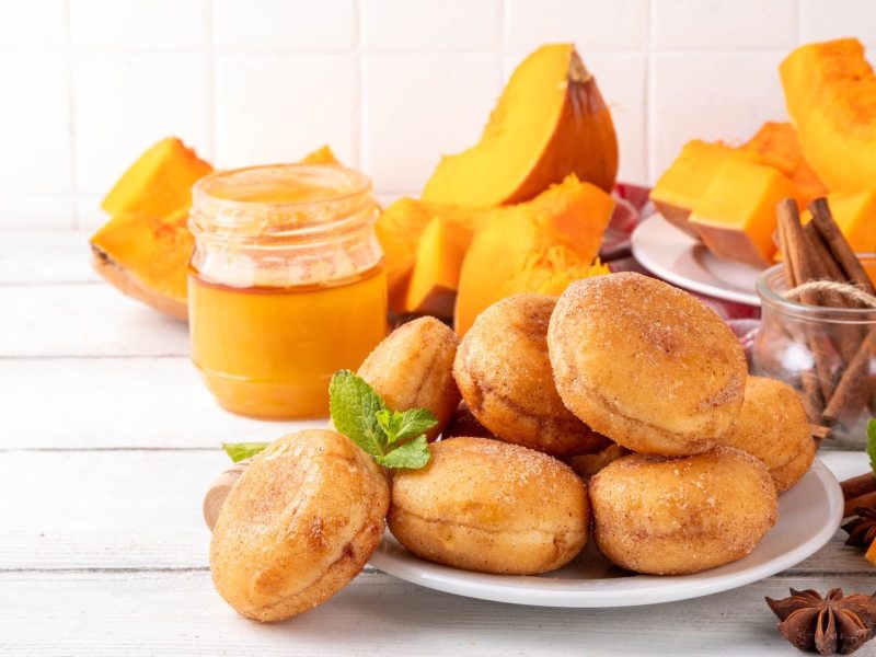 Ein Teller mit Kürbis-Krapfen aus dem Airfryer, dahinter einige Stücke Kürbis.