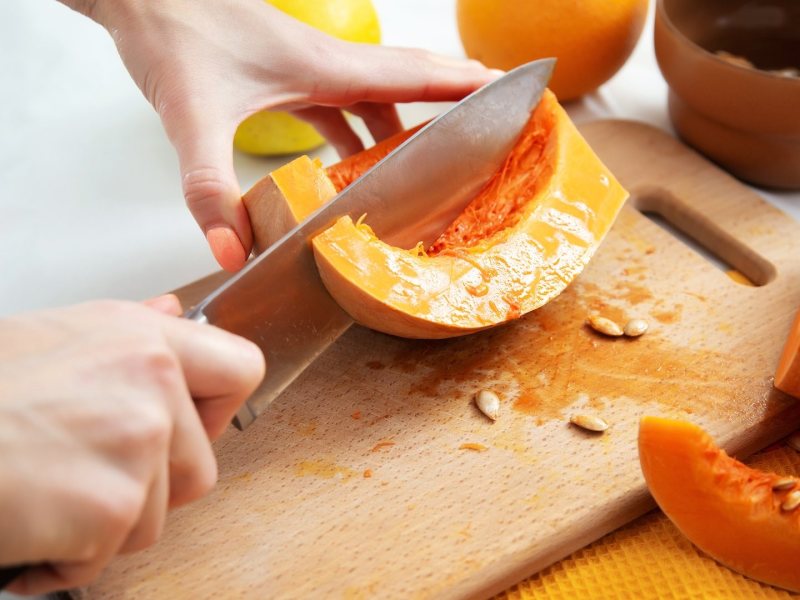 Kürbis schneiden: Eine Person halbiert ei Stück Kürbis.