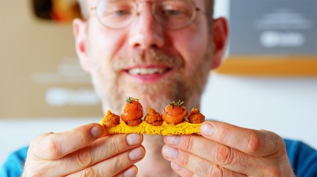 Ein Koch hält eine Kürbiswaffel mit Kürbispüree und Balsamico-Kirschen hoch.