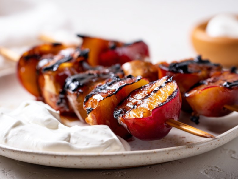 Zwei Spieße Pflaumen vom Grill mit Schlagsahne auf einem Teller.