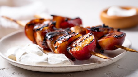 Zwei Spieße Pflaumen vom Grill mit Schlagsahne auf einem Teller.