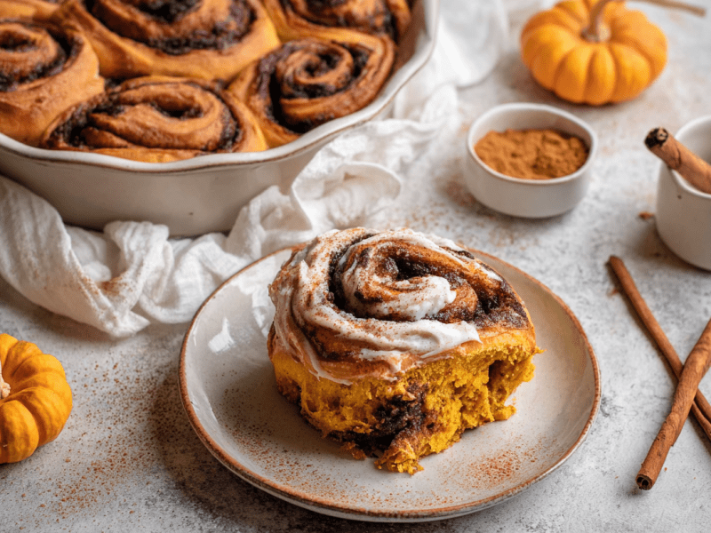 Pumpkin Spice Zimtschnecken in einer Backform, davor eine einzelne Zimtschnecke auf einem Teller.