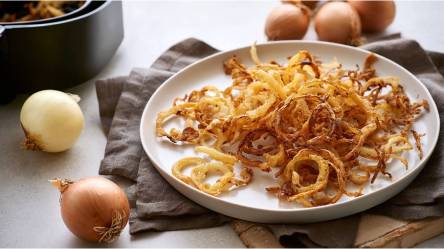 Schale mit Röstzwiebeln aus dem Airfryer, frische Zwiebeln und Airfryer im Hintergrund