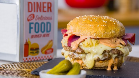 Ein Sauerkraut-Burger vor einem Serviettenspender, dazu Gewürzgurken.